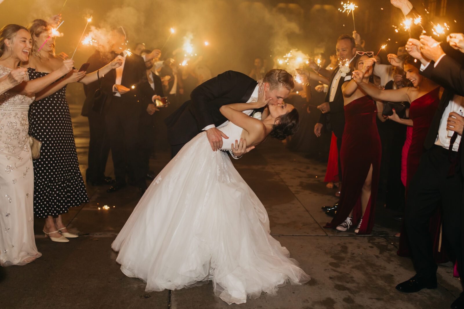 A lovely photo of the bride and groom sharing a kiss and being surrounded by their guests with sprinklers. 