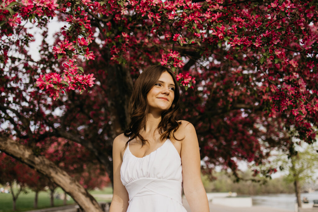 a photo of a senior wearing a white dress against a backdrop of a blossoming tree