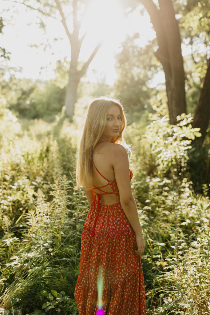 Meryl's high school senior photos taken in a field of greenery, wearing her vibrant red dress