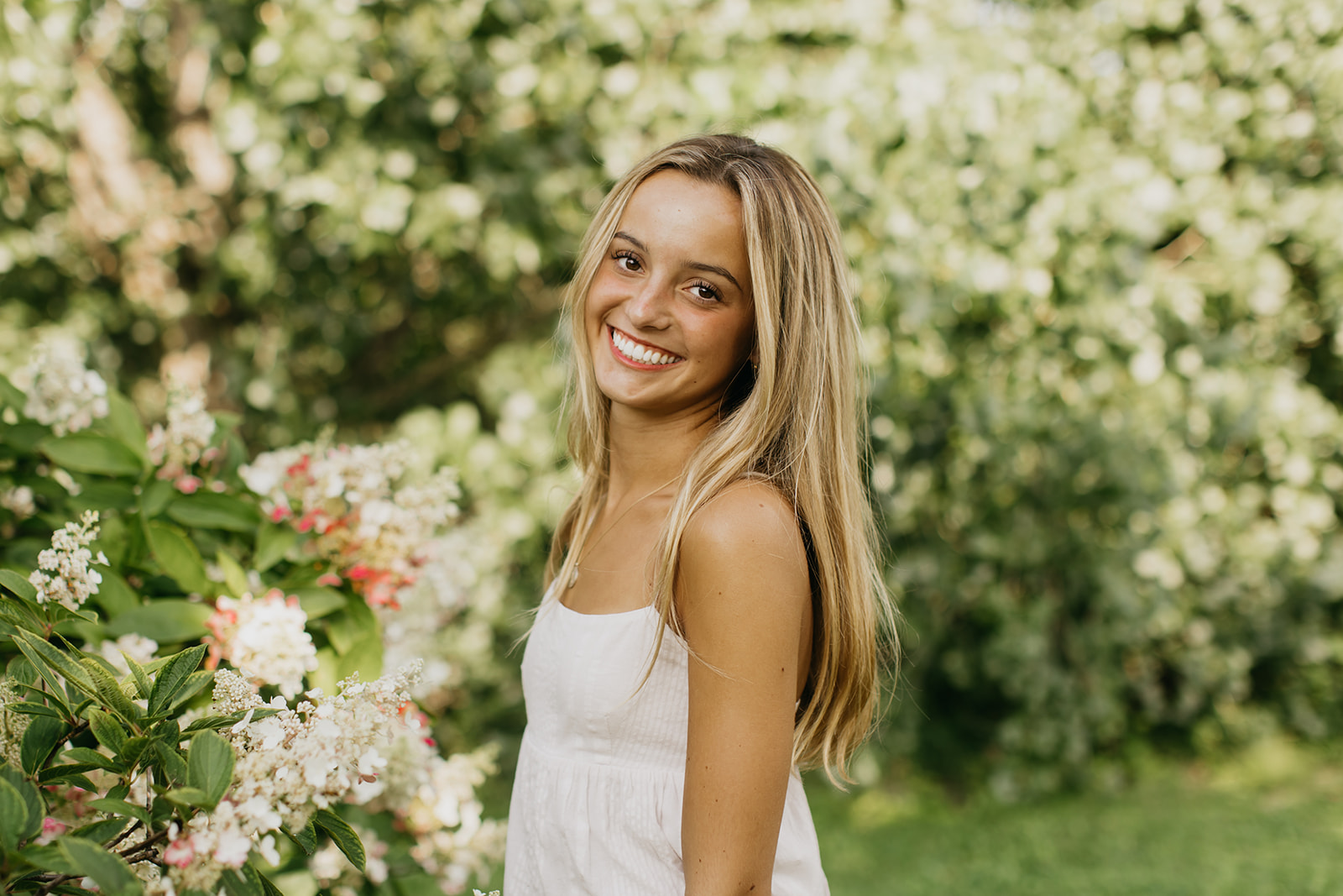 a photo of a breck high school senior with the green bushes and flowers as her background