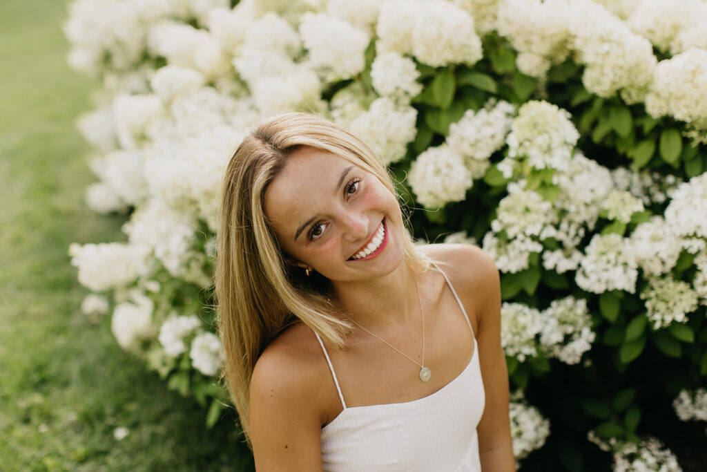 a photo of a breck high school senior with the green bushes and flowers as her background