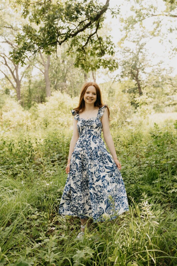 A photo of a high school senior wearing a dress with trees serving as the backdrop