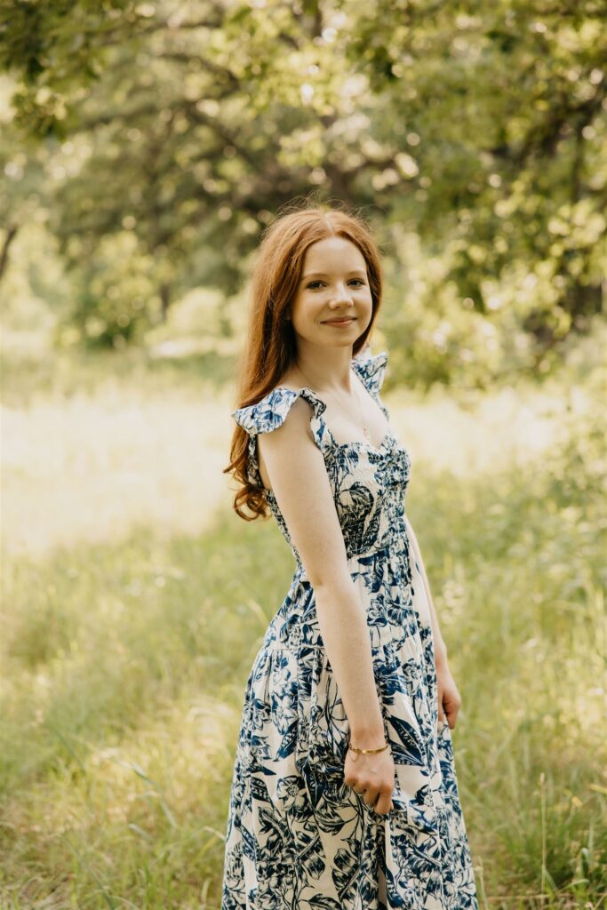 A photo of a high school senior wearing a dress with trees serving as the backdrop