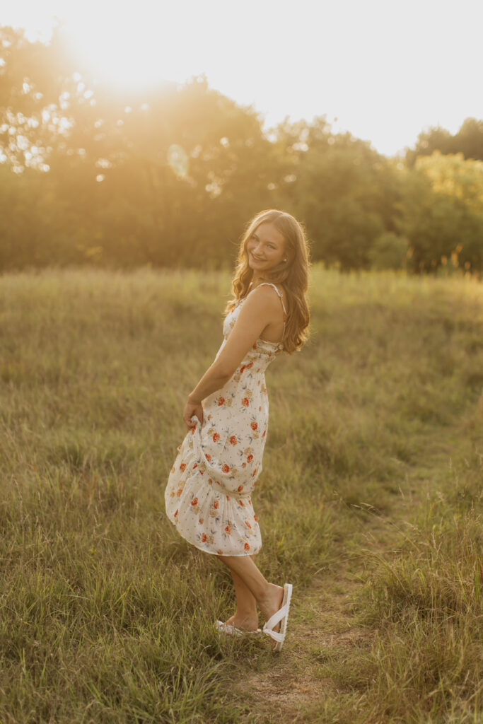 A photo of a senior,from Visitation School, MN, wearing a white, floral maxi dress taken during sunset 