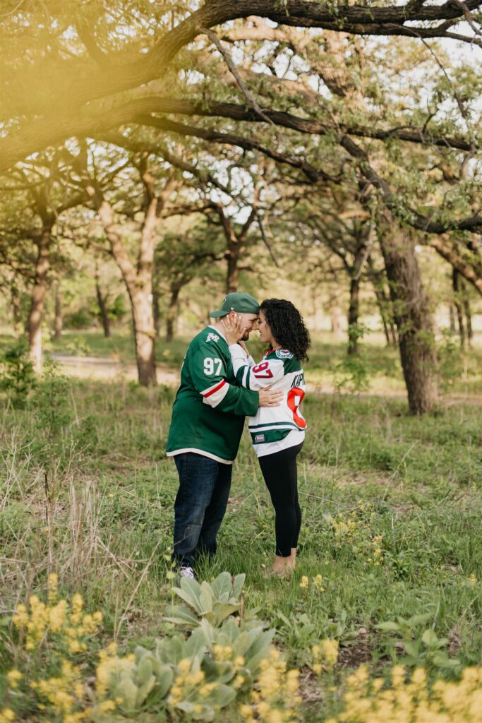 A photo of an engaged couple in a field surrounded by trees
