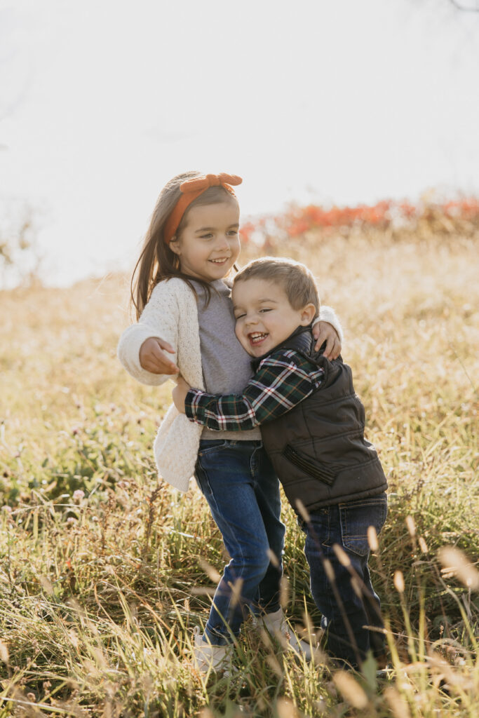 Young brother and sister hugging and smiling in a sunny Minnesota field during a fall family photo session.