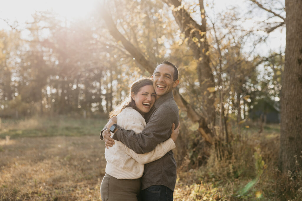  Parents hugging and laughing together in a golden, sunlit Minnesota forest during a fall family portrait session.