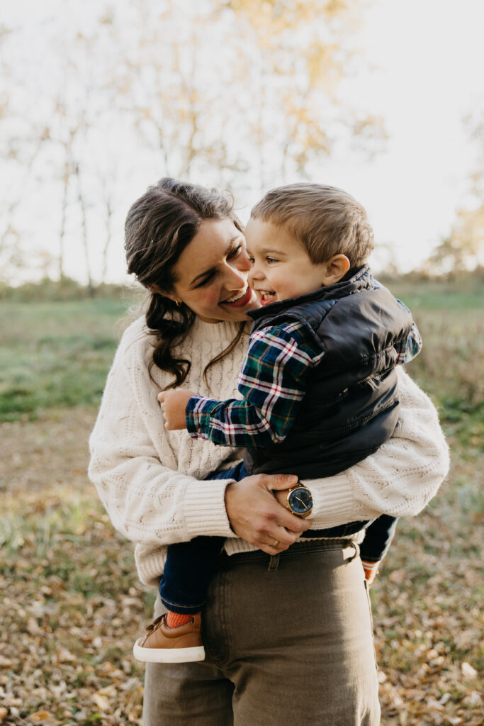 Mother holding her young son and smiling at him during a cozy fall family photo session in Minnesota.