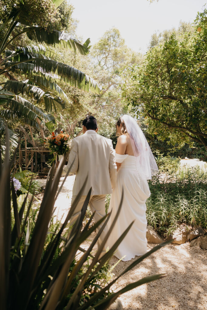 Bride and groom walking hand-in-hand through lush gardens at The Cole Home in Montecito during their private estate wedding.