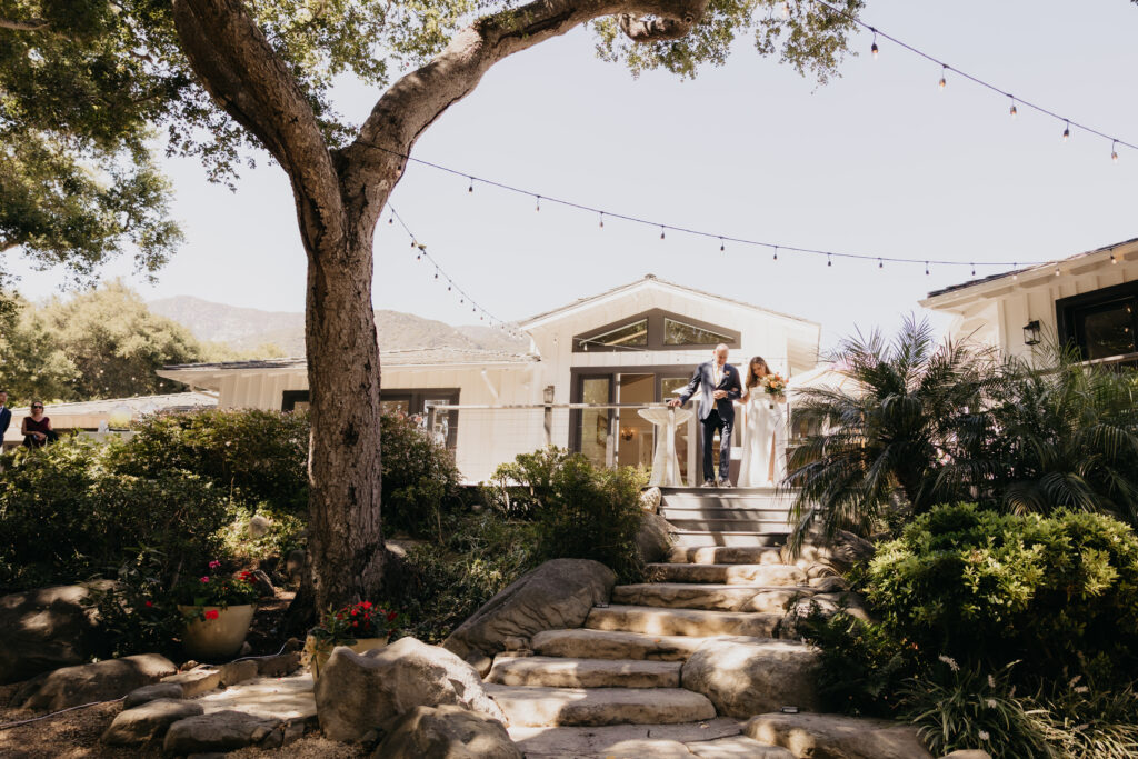 Bride walking down stone steps with her father at The Cole Home in Montecito for a private estate wedding ceremony.
