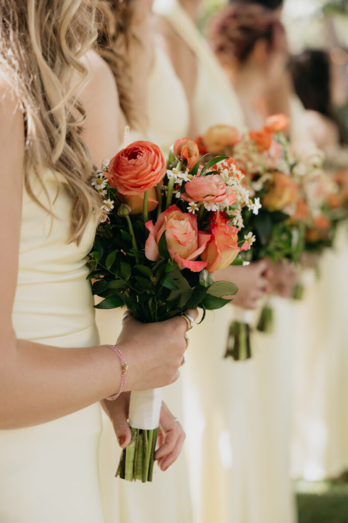 Bridesmaids in pale yellow dresses holding vibrant orange and coral bouquets during a Montecito private estate wedding.