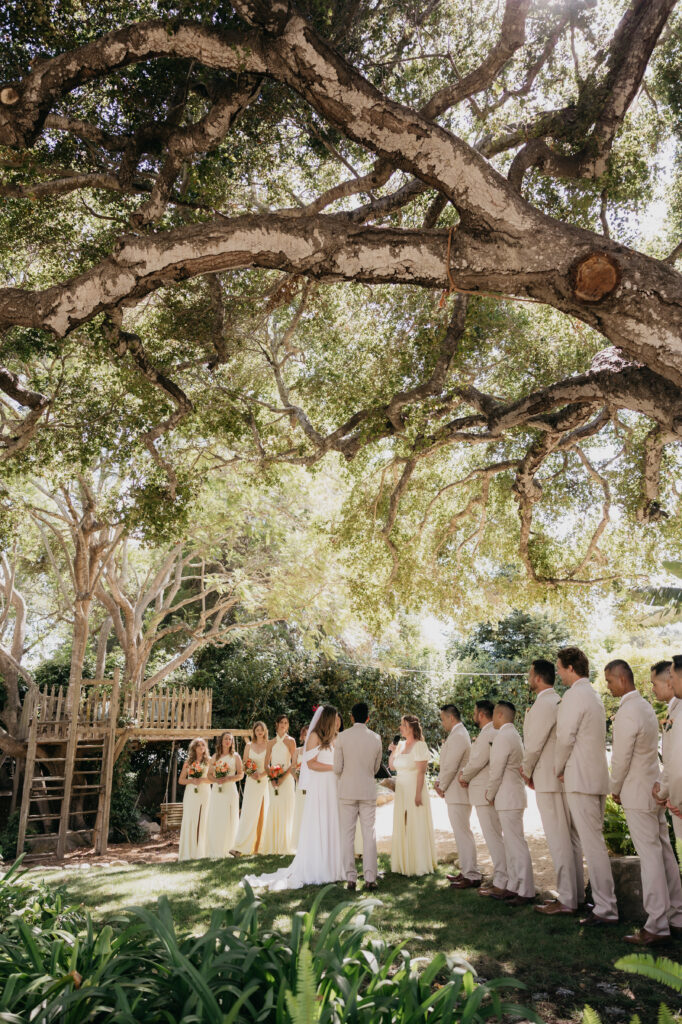 Bride and groom standing with their wedding party beneath oak trees during a Montecito private estate ceremony.