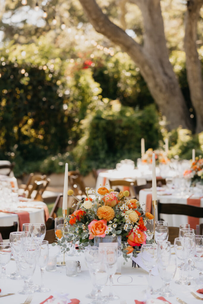 Close-up of a wedding reception table centerpiece with orange and coral florals at a Montecito private estate wedding.