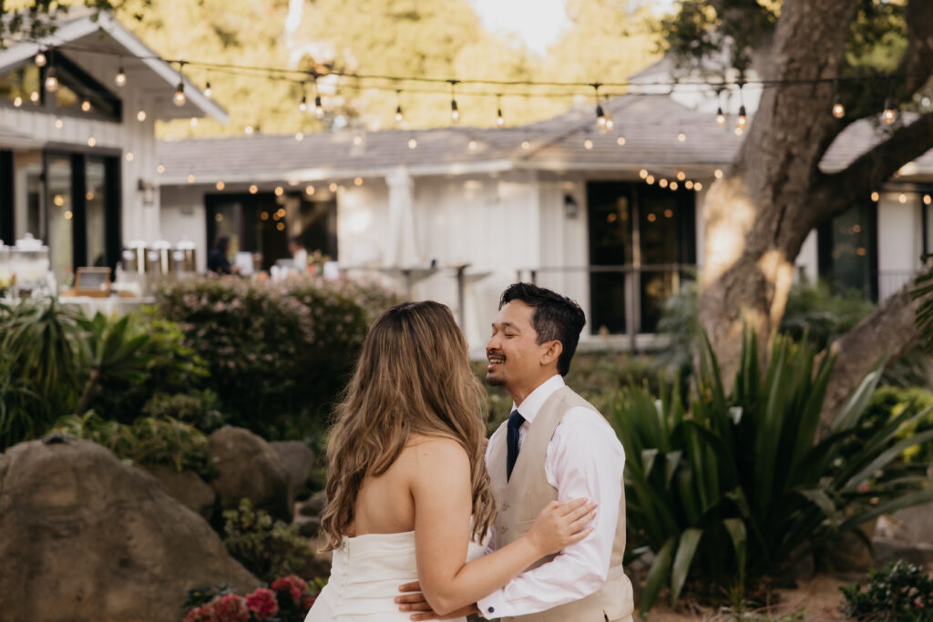 Couple smiling and holding each other closely during their first dance under string lights at a Montecito private estate.