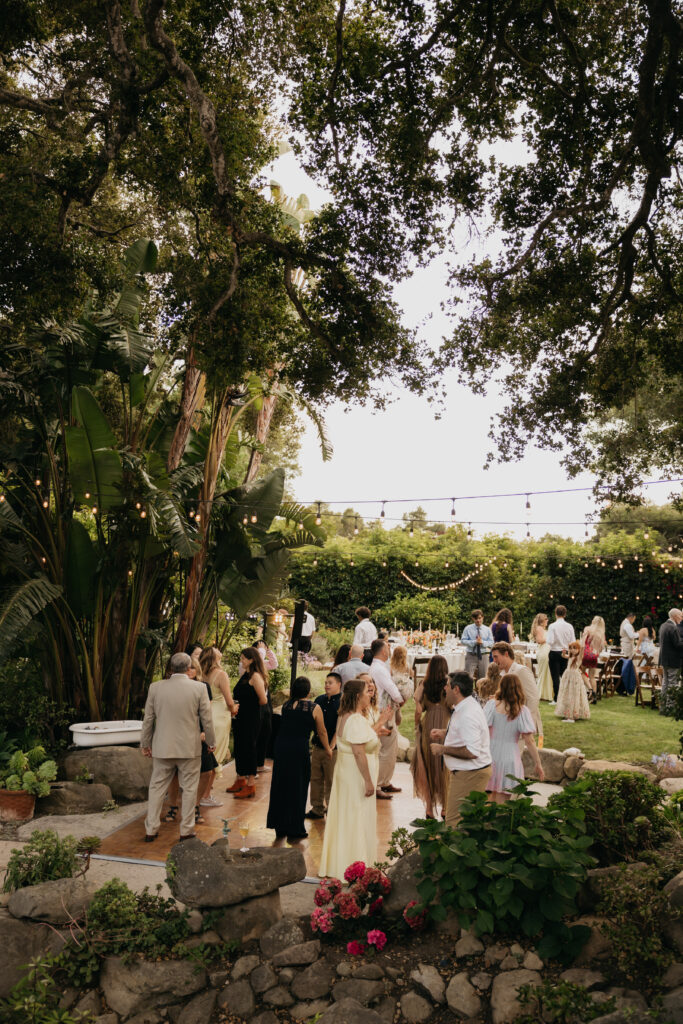 Guests mingling and dancing on the lawn surrounded by lush greenery during a Montecito private estate wedding reception.
