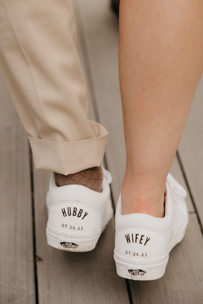 Close-up of custom white sneakers embroidered with “Hubby” and “Wifey” worn at a Montecito private estate wedding reception.