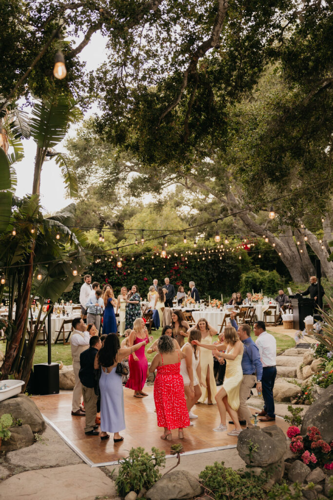 Wide view of guests dancing on the outdoor dance floor surrounded by oak trees at a Montecito estate wedding.