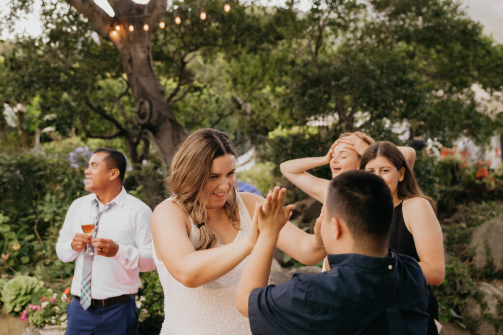 Bride in a short reception dress playing a hand game with a young guest at a Montecito private estate wedding.