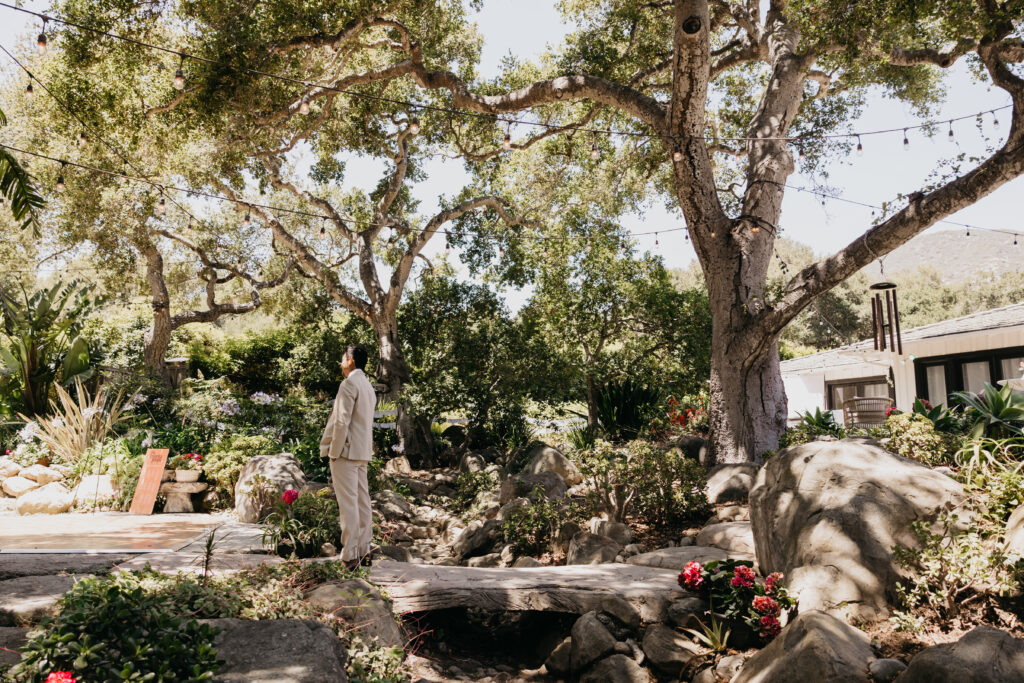 Groom waiting on a stone pathway surrounded by oak trees for the first look at a Montecito private estate wedding.