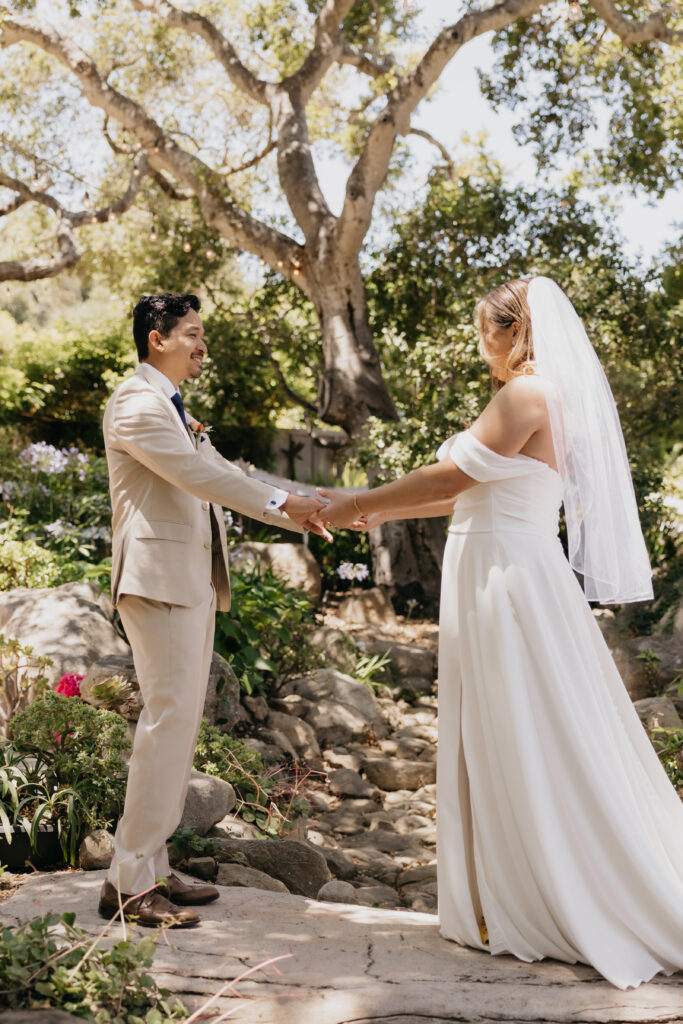 Bride and groom holding hands and smiling during their first look at a Montecito private estate wedding.