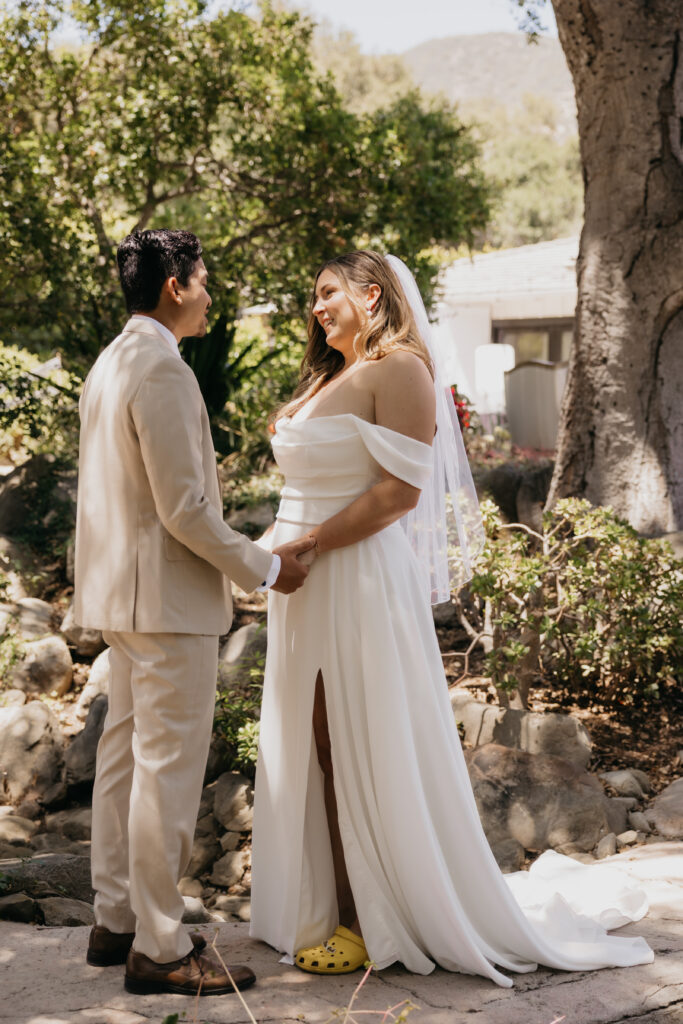 Bride smiling in her off-the-shoulder gown while the groom gazes at her during their first look at The Cole Home in Montecito.