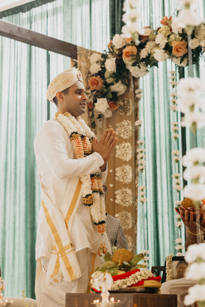 Groom Sanjay standing with folded hands during traditional Indian wedding rituals under floral mandap at Renaissance Depot