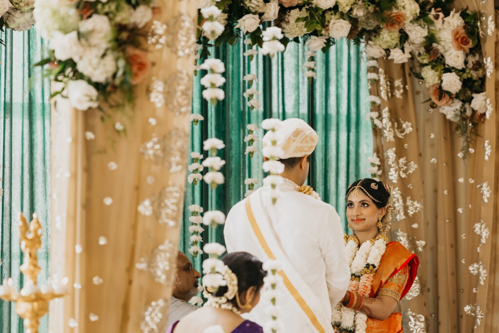 Groom facing bride during sacred wedding ceremony surrounded by jasmine garlands and floral mandap decor