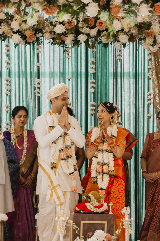 Bride and groom smiling and exchanging Namaste during Indian wedding ceremony under floral mandap in Minneapolis | Mycah Bain Photography