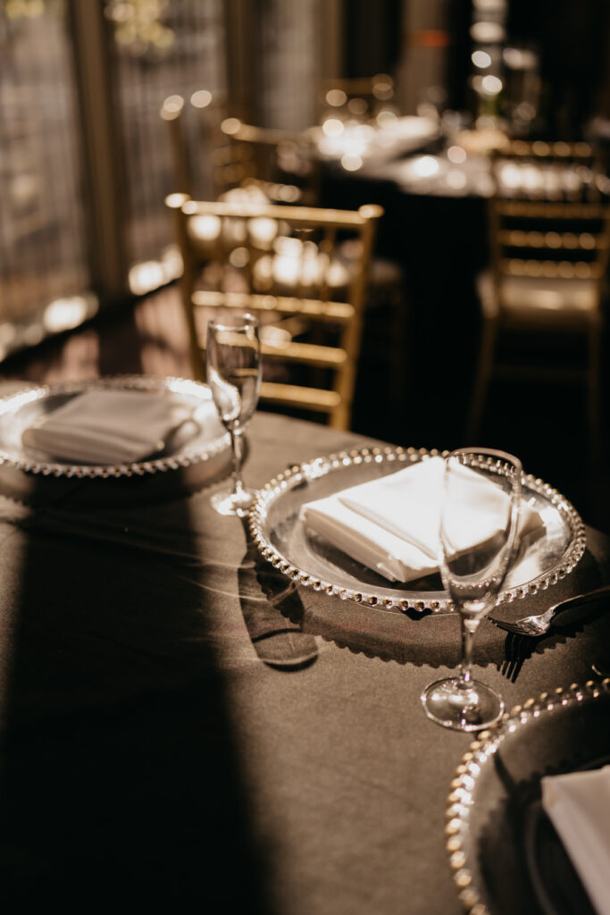 Close-up of reception table setting with glass chargers, black linens, and candlelight at Renaissance Depot wedding | Mycah Bain Photography.
