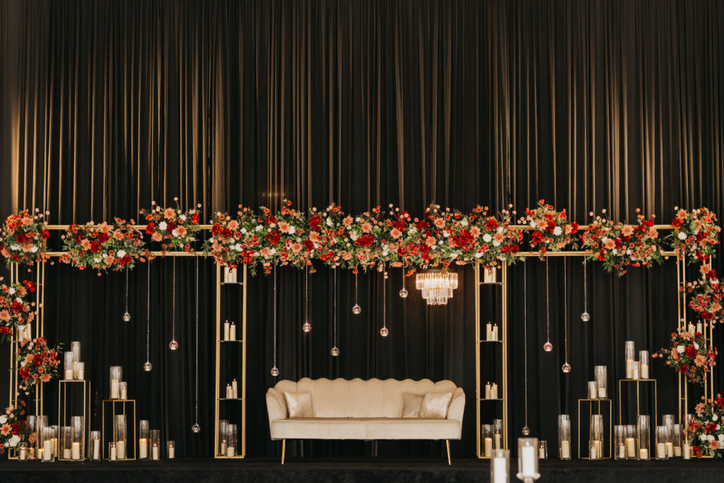 Reception stage with white loveseat, black draping, floral garlands, and chandeliers at Renaissance Depot wedding | Mycah Bain Photography.
