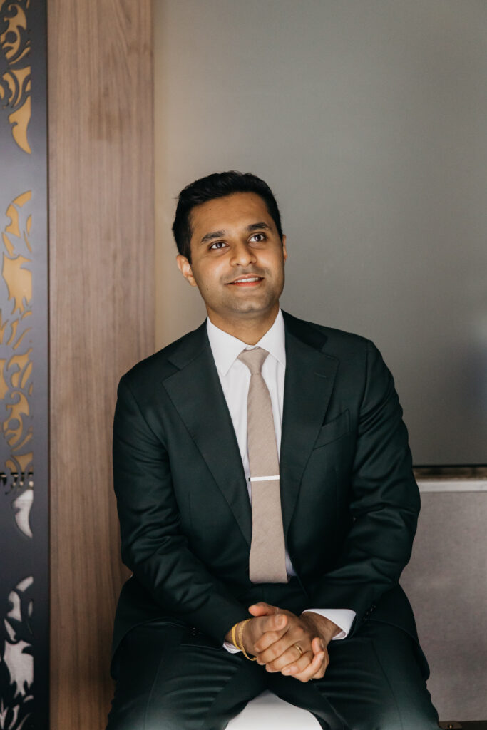 Groom Sanjay in classic black suit and tie, seated before his wedding reception at Renaissance Depot Minneapolis | Mycah Bain Photography, traditional wedding photographer.