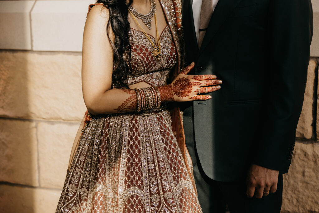 Bride’s mehndi-decorated hand resting on groom’s suit during Indian wedding reception at Renaissance Depot, captured by Mycah Bain Photography, traditional wedding photographer.