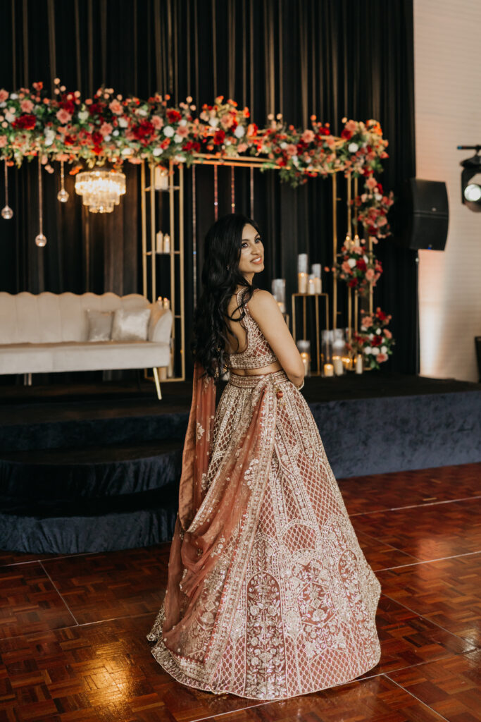 Bride Apoorva in sparkling lehenga, posing on the dance floor with floral stage backdrop at Renaissance Depot reception | Mycah Bain Photography.