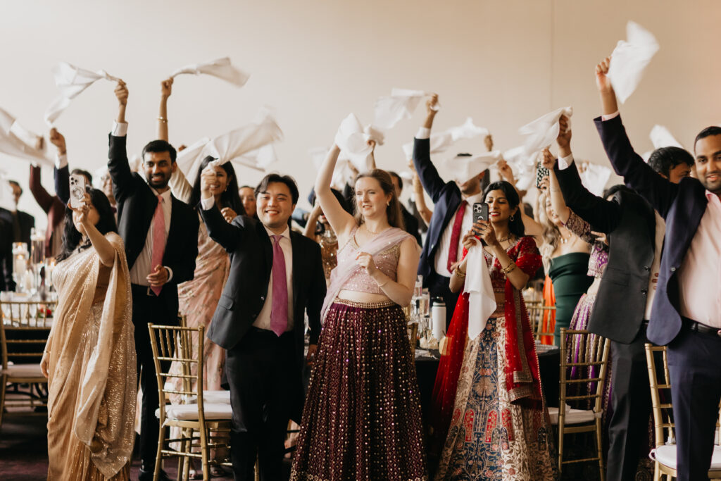 Wedding guests waving napkins and cheering during Apoorva and Sanjay’s grand reception entrance at Renaissance Depot Minneapolis | Mycah Bain Photography.