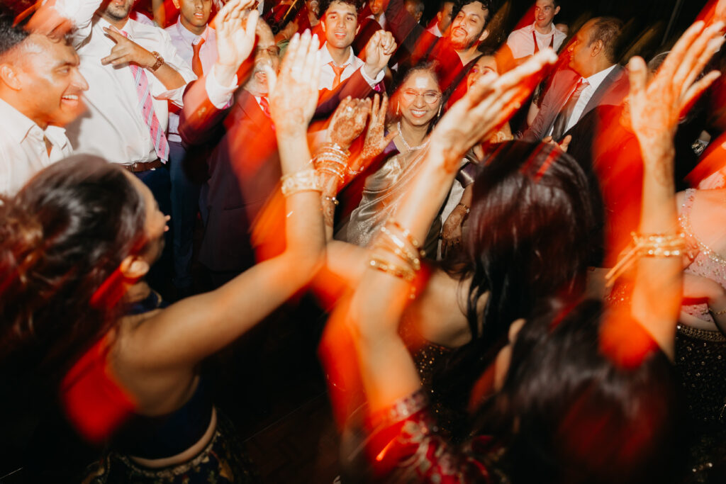 Guests dancing with raised hands on a packed dance floor during Apoorva and Sanjay’s Indian wedding reception in Minneapolis | Mycah Bain Photography.