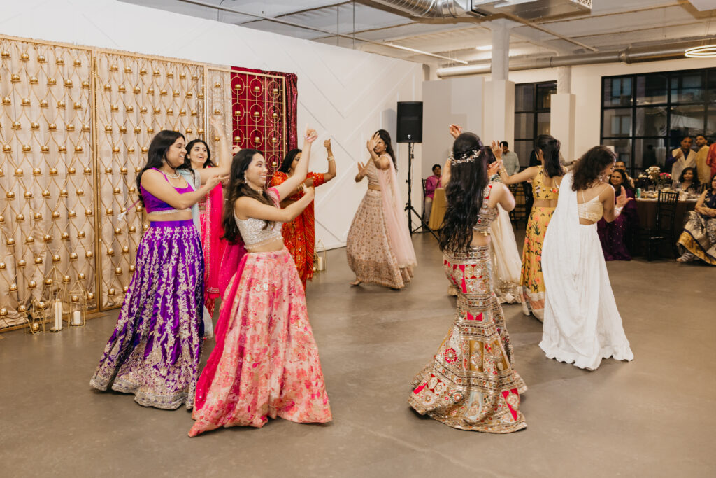 Group of wedding guests dancing together in colorful Indian outfits during a lively sangeet performance, with smiles and synchronized movements