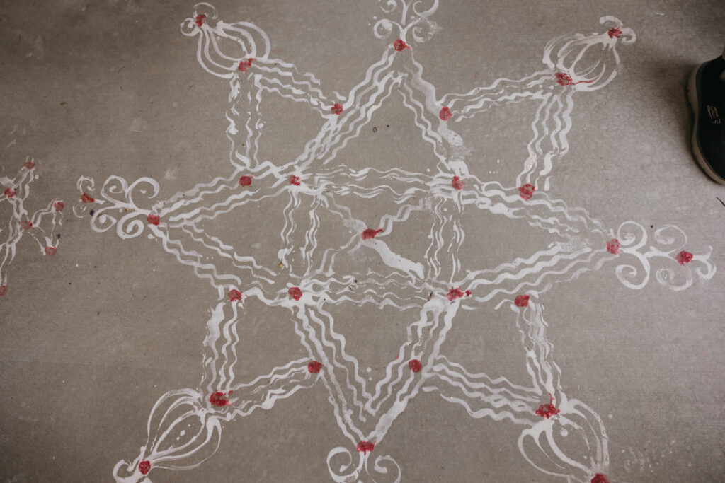 Close-up of intricate white and red rangoli pattern at entrance during Var Pooja Indian wedding ceremony