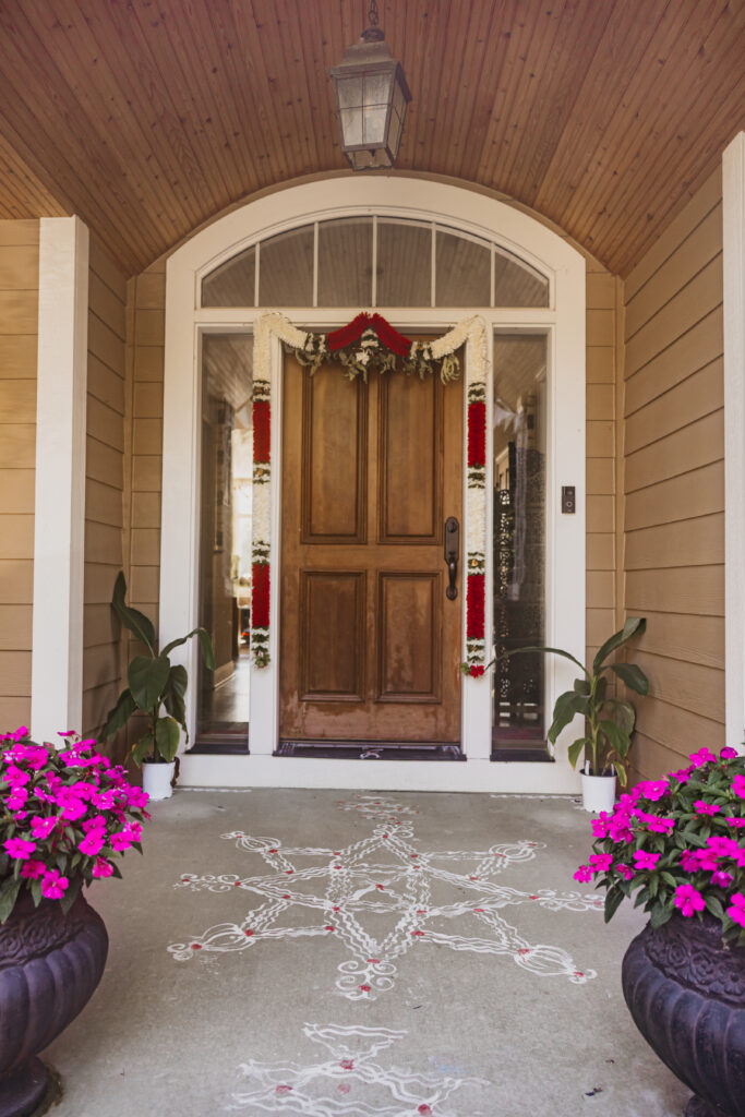 Front entrance of bride’s family home adorned with rangoli and flowers welcoming groom’s family for Var Pooja