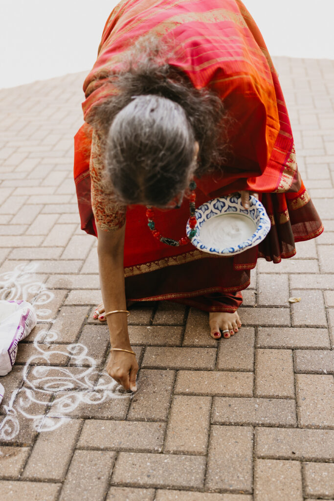 Woman in traditional red saree creating rangoli design on brick pathway during Var Pooja ceremony