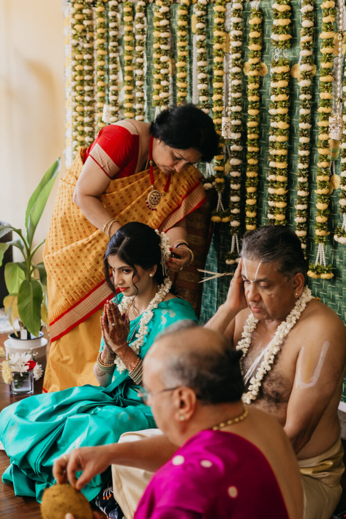 Bride seated in turquoise saree with father and relatives performing sacred blessings during Var Pooja