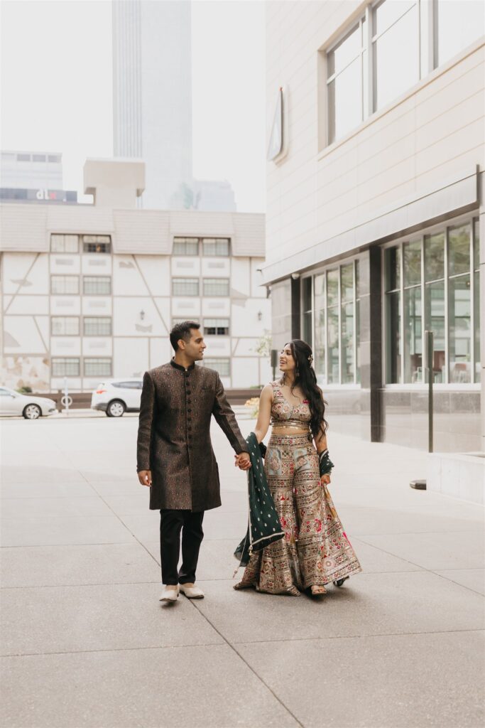 Indian couple walking hand-in-hand through downtown Minneapolis during their wedding weekend, dressed in traditional embroidered attire