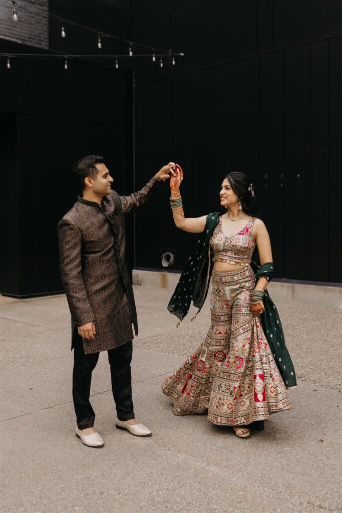 Groom twirling the bride outdoors during their wedding portraits, with the bride’s lehenga swirling as she smiles beneath string lights