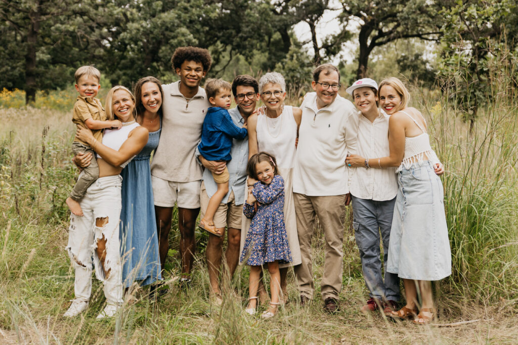 Large multi-generational family standing close together and smiling in a grassy Minnesota field during a summer family photo session.