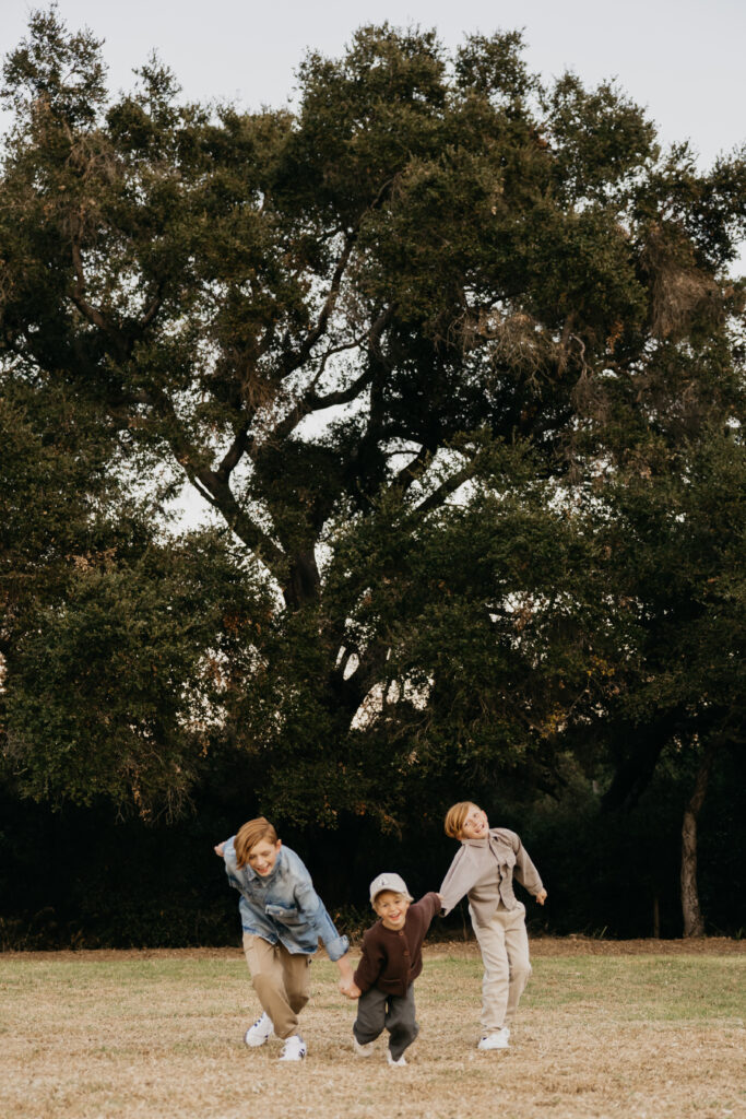 Three siblings running and laughing together across an open grassy field during a family photo session in Minnesota.