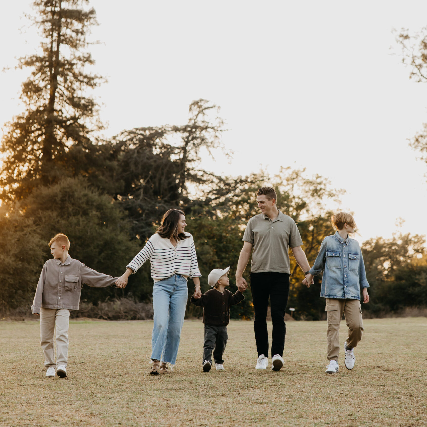 Family of five walking hand in hand across a sunny Minnesota field during a relaxed fall family photo session.