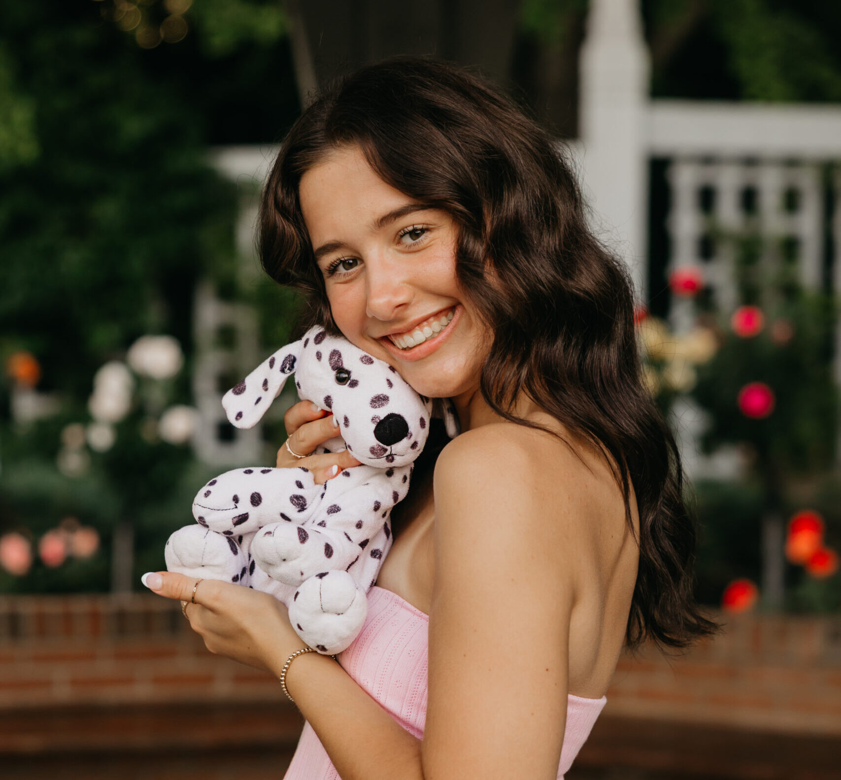 Senior girl in a pink top and white pants smiling while holding her Dalmatian stuffed animal during her Minneapolis senior photos with Mycah Bain Photography.