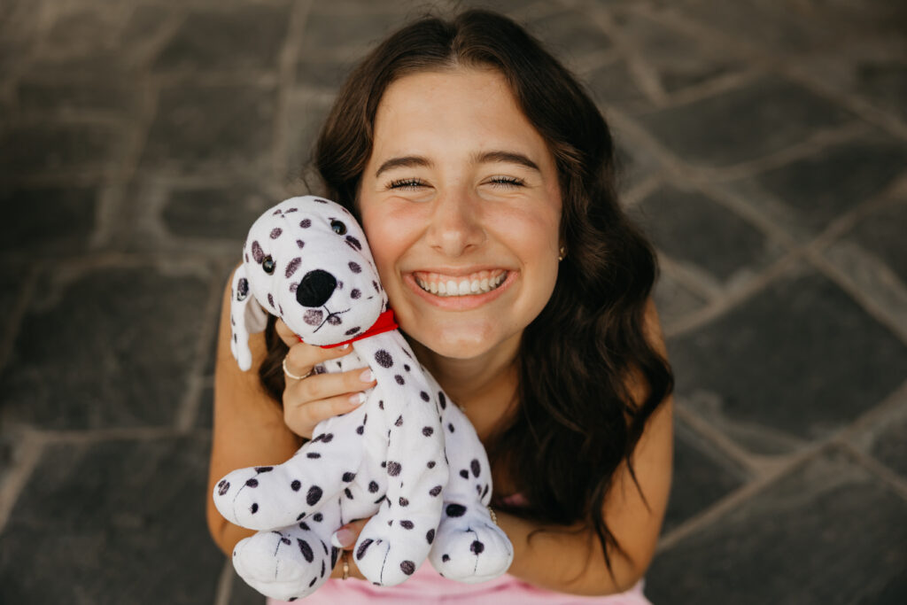 Close-up of senior girl laughing and cuddling a Dalmatian stuffed toy, capturing playful and nostalgic vibes during her Minneapolis senior photo session with Mycah Bain Photography.