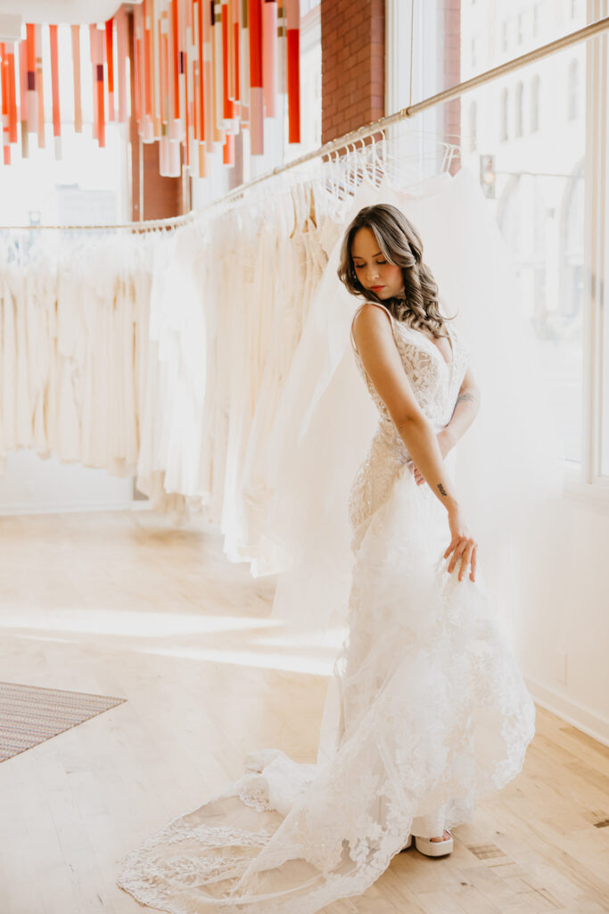 Bride in a lace V-neck gown gently holding her train during a bridal fitting at Vow’d Weddings in Minneapolis.