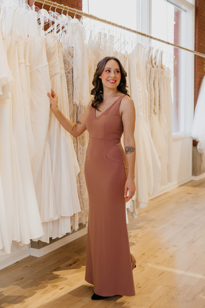 Bridesmaid in a mauve V-neck gown smiles while browsing bridal gowns at Vow’d Weddings boutique in Minneapolis.