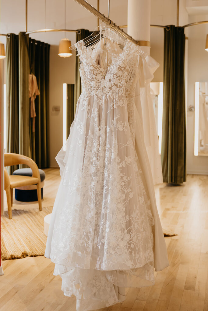Elegant lace bridal gown with floral details displayed in the Minneapolis Vow’d Weddings boutique, photographed by Mycah Bain Photography.